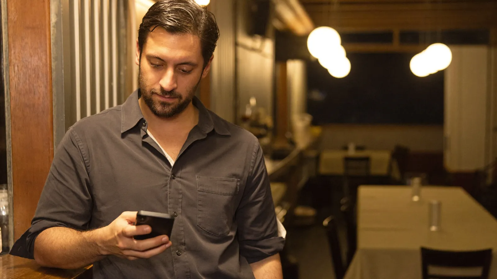 El encargado, en la barra del local, lee un aviso en su teléfono.